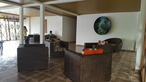 A spacious lobby with wicker furniture, a large painting on the wall, and a tiled floor. - Reserva Natural Yavary Tucano (Leticia)
