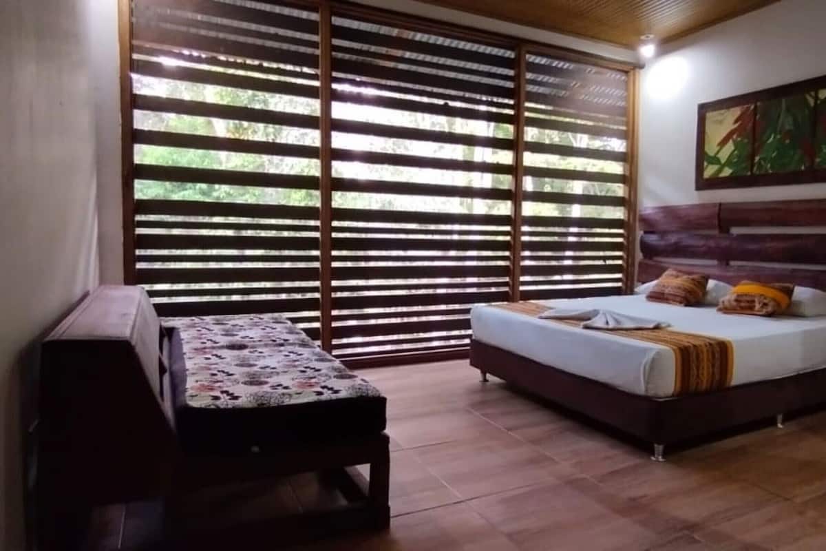 Une chambre à coucher avec un lit, un banc, une fenêtre avec des stores et un tableau au mur.