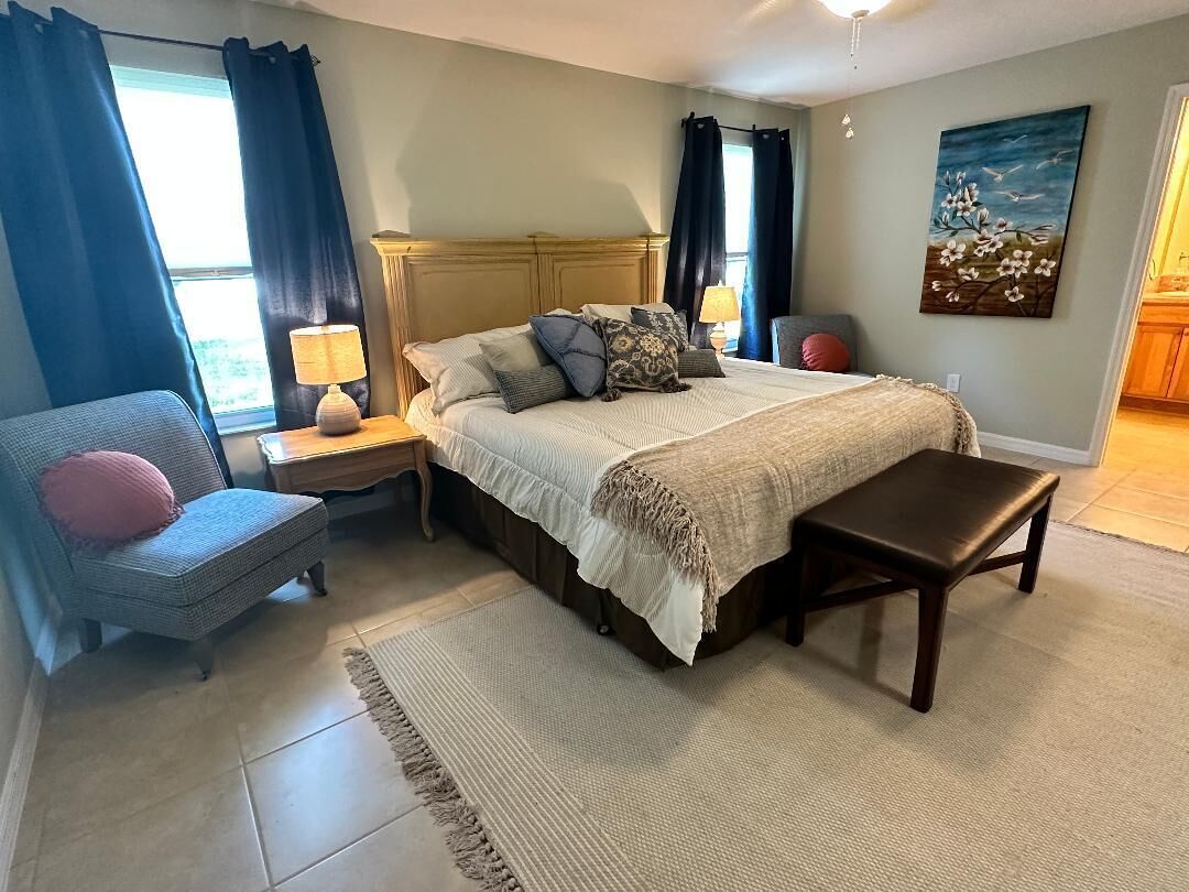 Une chambre à coucher comprenant un lit, des tables de chevet, une chaise, un banc, un tapis et un tableau accroché au mur.