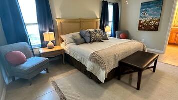 Une chambre à coucher comprenant un lit, des tables de chevet, une chaise, un banc, un tapis et un tableau accroché au mur.