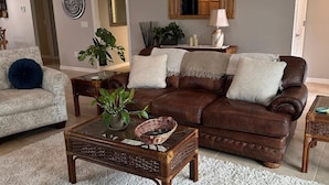 A living room with a brown leather sofa, a patterned armchair, a glass coffee table, and a white shag rug. - Rare find in Historic Orange Blossom 3/2 with golf cart (Lady Lake)