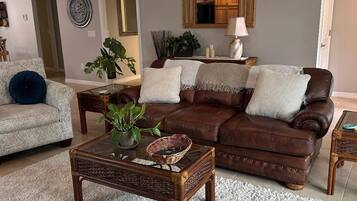 Un salon avec un canapé en cuir marron, un fauteuil à motifs, une table basse en verre et un tapis à poils longs blanc.