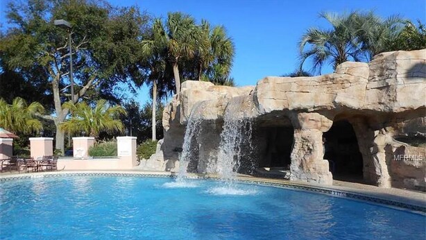 A swimming pool with a waterfall feature, surrounded by palm trees and a rocky structure. - Rare find in Historic Orange Blossom 3/2 with golf cart (Lady Lake)