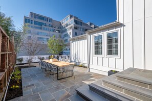 Eine Terrasse mit Holztisch und -stühlen, Steinböden und einem kleinen Gartenbereich.