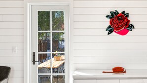 Una puerta blanca con un panel de vidrio, una mesa de madera con sillas y un teléfono rojo sobre un estante blanco.