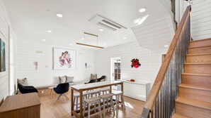 Un interior moderno con una escalera de madera, una zona de comedor con taburetes y un aire acondicionado instalado en la pared.