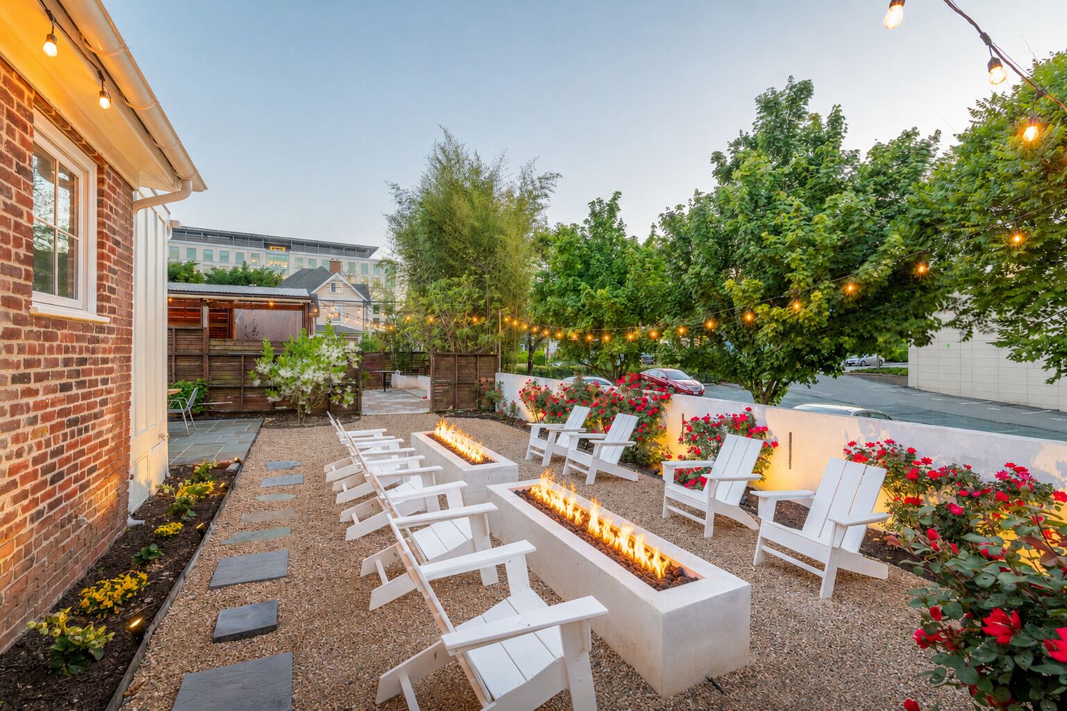 A patio with white chairs, a fire feature, and string lights.