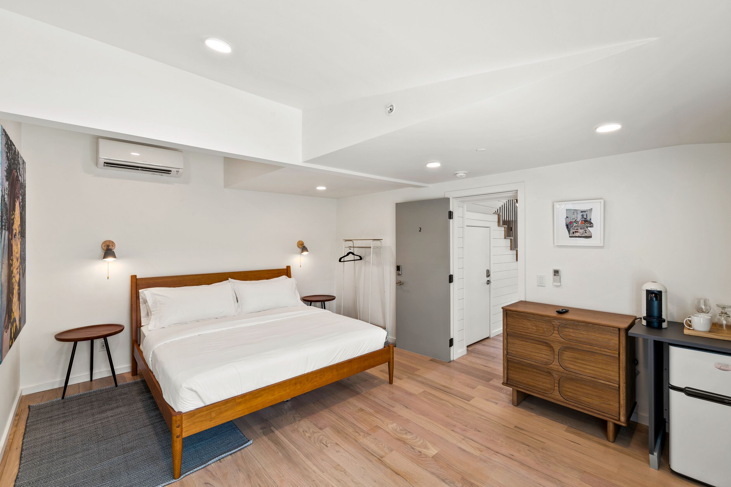 Un dormitorio moderno con una cama de madera, un aparador, un escritorio con cafetera y un perchero.