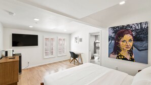 A modern hotel room with a large bed, a desk, a flat-screen TV, and a painting on the wall.