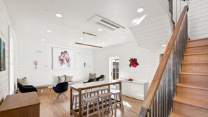 A modern interior with a wooden staircase, a dining area with stools, and a white wall with decorative elements.