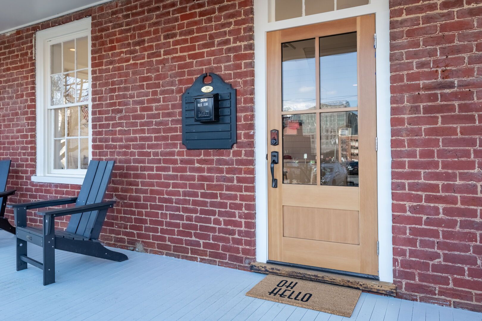 A brick building with a wooden door and a mailbox. There are two Adirondack chairs outside.
