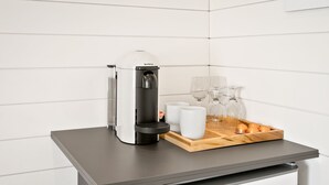 A compact kitchen area with a coffee machine, a tray with cups and glasses, and a refrigerator with a sticker.