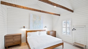 A bedroom with a wooden bed, two nightstands, a dresser, a hanging rack, and a large abstract painting on the wall.