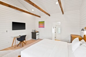 Une chambre moderne comprenant un lit, un bureau, une chaise, un téléviseur et une petite kitchenette.