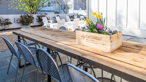 A wooden table with metal chairs, a wooden crate with flowers, and a white fence in an outdoor setting.