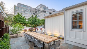 Eine Terrasse mit Holztisch und Metallstühlen, umgeben von Steinplatten und Grünpflanzen.