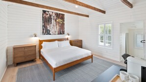 Ein Schlafzimmer mit einem hölzernen Bett, weißen Wänden, einem großen abstrakten Gemälde und einem kleinen Schreibtisch mit Stuhl.