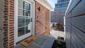 A brick exterior with a white door and a doormat with "WELCOME" written on it. - Pet Friendly Boutique Hotel Room, Walk to Downtown | Rose Jean Room 5 (Charlottesville)
