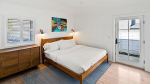 A bedroom with a wooden bed, a dresser, a painting on the wall, and a door with a view of the outside. - Pet Friendly Boutique Hotel Room, Walk to Downtown | Rose Jean Room 5 (Charlottesville)