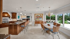 Une cuisine spacieuse dotée d’un grand îlot central, de meubles en bois et d’un coin repas avec des chaises en osier et une table en marbre.