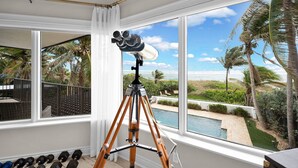 Ein Zimmer mit einem Teleskop auf einem Stativ, große Fenster mit Blick auf einen Pool und Palmen.