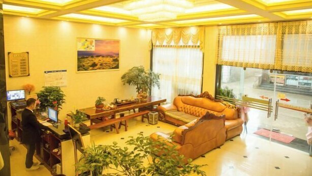 A hotel lobby with a sofa, a desk with a computer, a plant, and a painting on the wall. - Longge Express Inn (Luoping)
