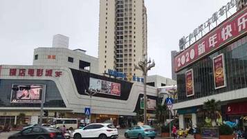 A modern building with a curved facade, large digital billboards, and a prominent red sign on the right.
