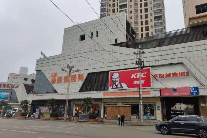 A KFC restaurant with a prominent red and white logo, a parking sign, and a building with a unique angular design.