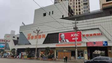 A KFC restaurant with a prominent red and white logo, a parking sign, and a building with a unique angular design.