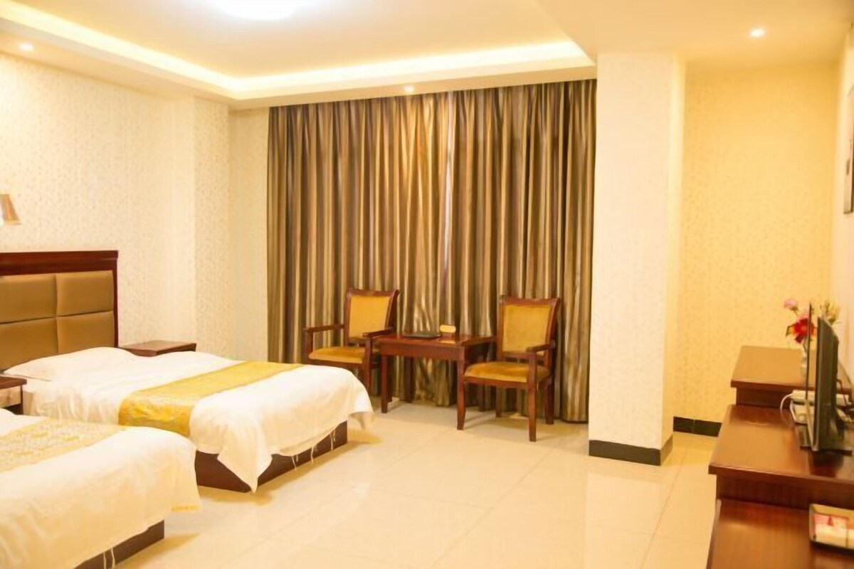 Quarto de hotel com duas camas, uma escrivaninha, uma cadeira e uma cortina.