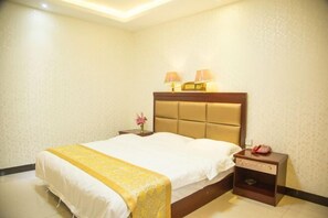 Quarto de hotel com uma cama grande, mesa de cabeceira com abajur e uma pequena mesa com telefone.