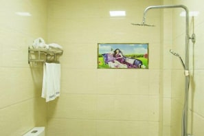 Um chuveiro com porta de vidro, um porta-toalhas com uma toalha branca, e uma imagem de uma mulher num vestido roxo na parede.