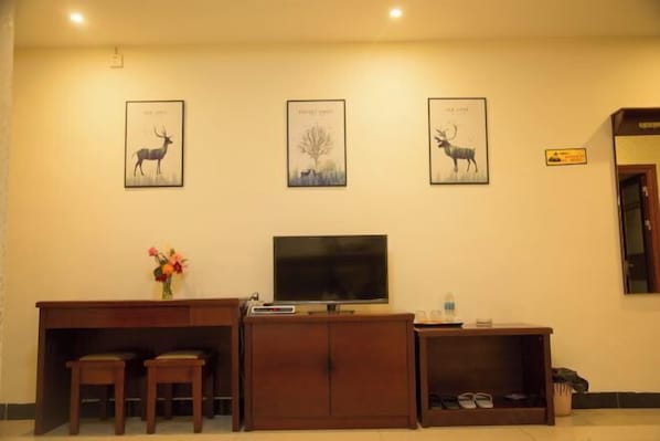 Uma área de recepção de hotel com uma mesa de madeira, duas cadeiras, uma TV de tela plana e três quadros na parede.