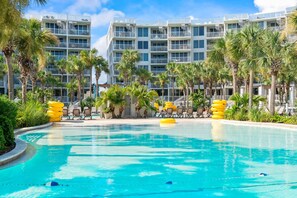 Ein Swimmingpool mit Liegestühlen und gelben Schwimmhilfen, umgeben von Palmen und einem mehrstöckigen Gebäude mit Balkonen.
