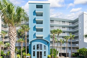 Ein modernes, mehrgeschossiges Hotel mit einer markanten, blauen Fassade, mehreren Balkonen und umliegenden Palmen.