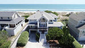 A large two-story house with a front porch, a covered entryway, and a staircase leading to the main entrance. - Ocean Views, Den, Community Pools, Close to Beach access, 103, Brigadune-Oceanfront (Corolla)