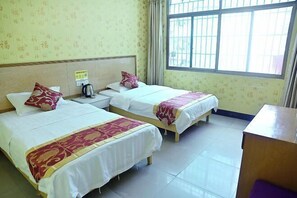 Habitación de hotel con dos camas, una mesita de noche de madera, una tetera y una ventana con barrotes.