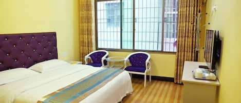 Habitación de hotel con cama, dos sillas, una mesita, televisor y ventana con cortinas.