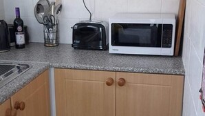 Una cocina con tostadora, microondas, una botella de vino y un recipiente para utensilios sobre la encimera.