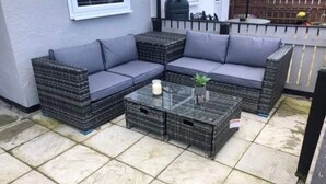 Un patio con un sofá modular, una mesa de centro de vidrio y cajas de almacenamiento.