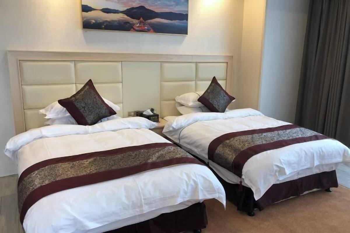 A hotel room with two beds, each with white bedding and brown decorative pillows.
