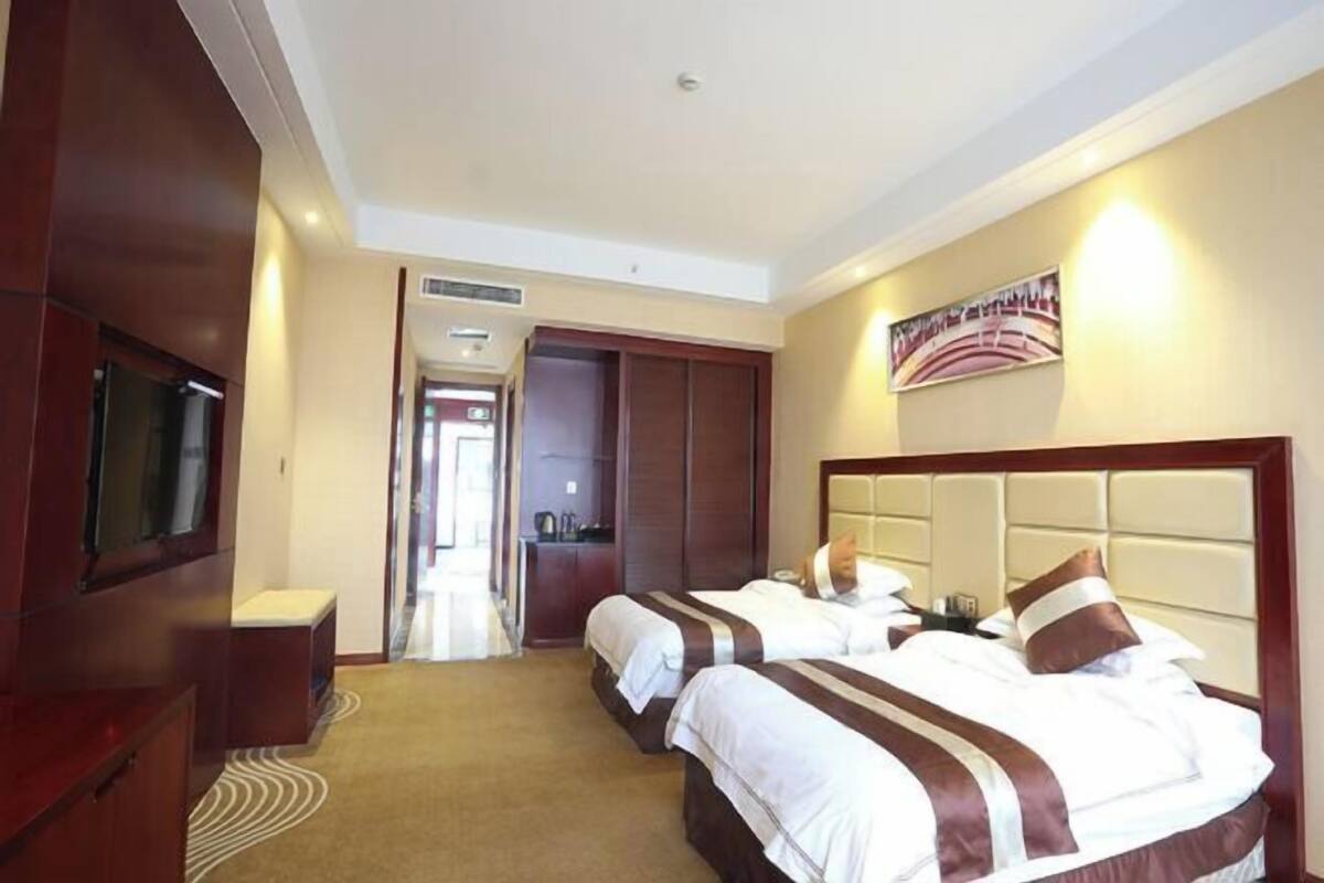 A hotel room with two beds, a television, a wardrobe, and a painting on the wall.