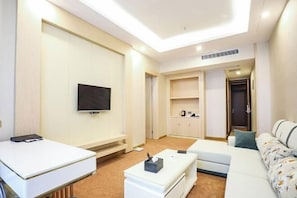A modern hotel room with a flat-screen TV, a sofa, a small table, and a kitchenette area.