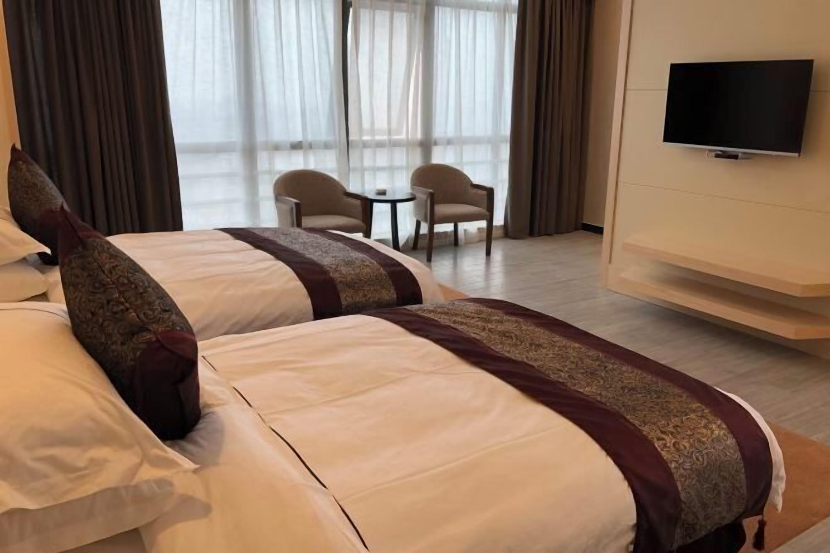 A hotel room with two beds, a TV, and a view of the outdoors.