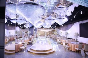 A banquet hall with round tables and chairs, a stage, and a large chandelier.