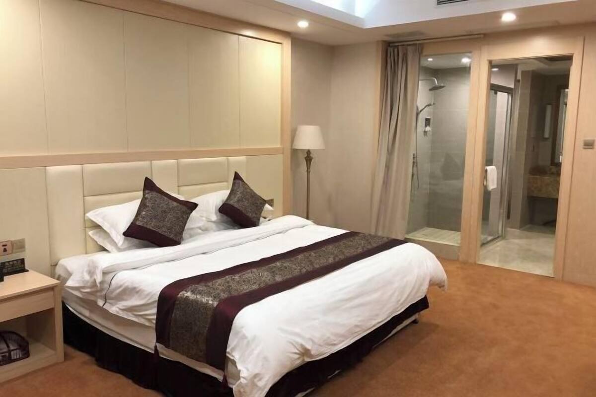 A hotel room with a bed, a nightstand, a lamp, a shower area, and a glass door leading to a bathroom.