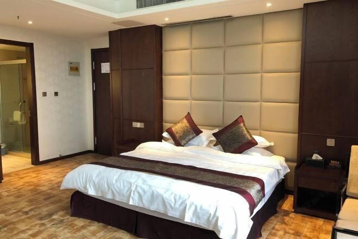 A hotel room with a large bed, a wooden wardrobe, and a glass shower area.