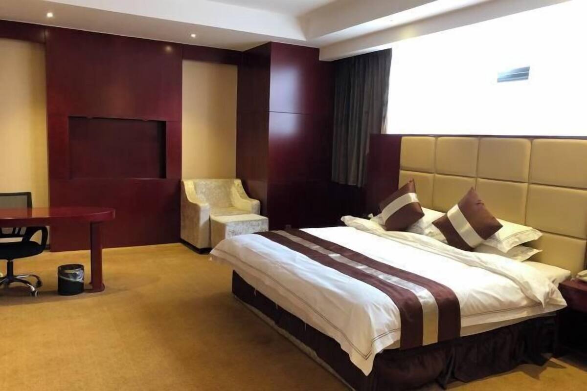 A hotel room with a large bed, a desk, a chair, and a small table.