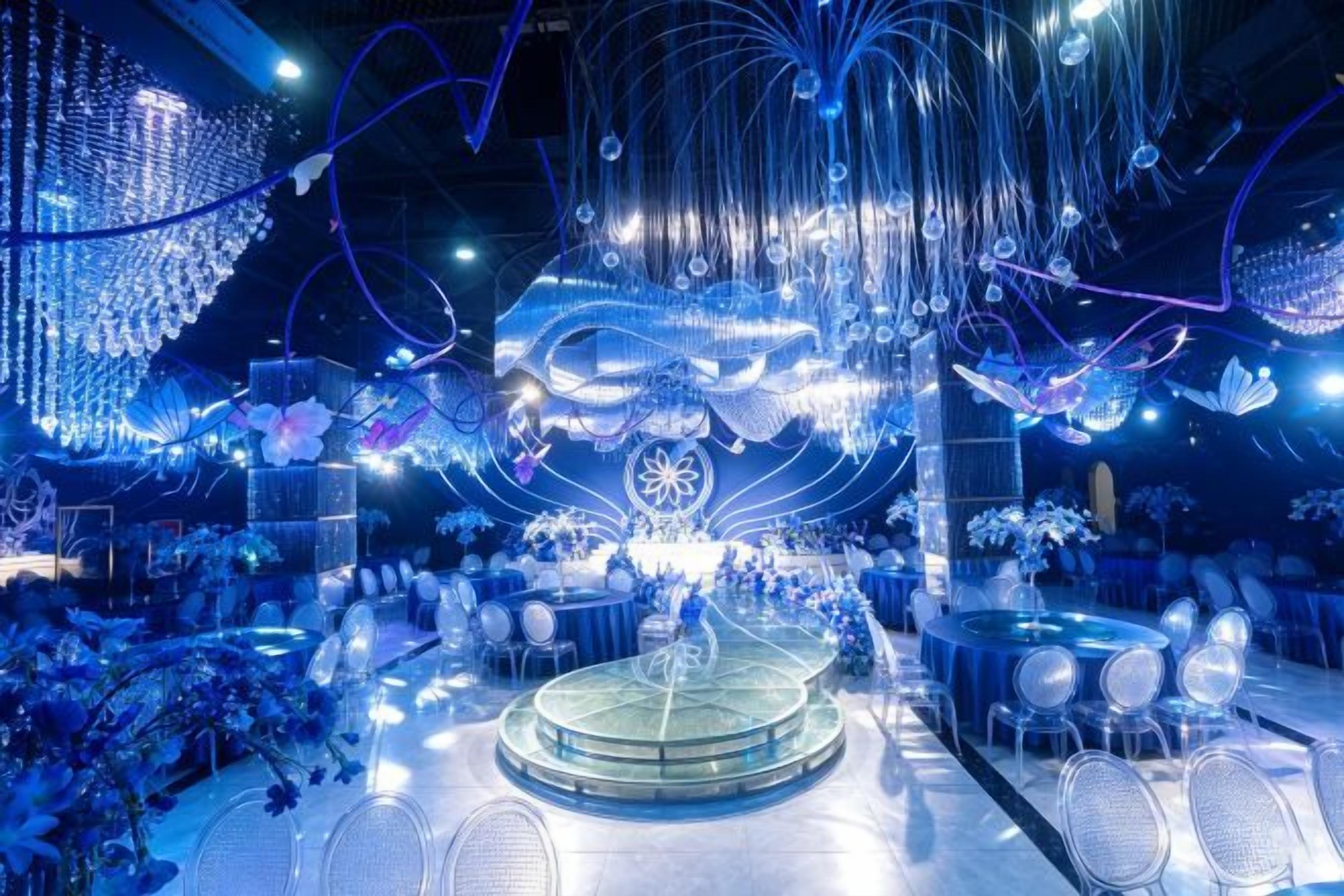 A venue with round tables and chairs, a central stage, and hanging decorations.