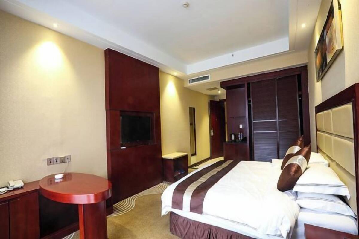 A hotel room with a bed, a round table, a TV, and a wardrobe.